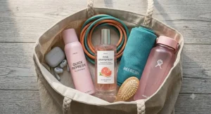 A flat lay of summer gym bag essentials including pink grapefruit eau de parfum, dry shampoo, and resistance bands.
